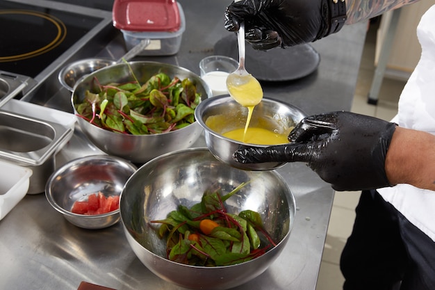 Close-up van chef-kokhanden die salade gietende saus in een restaurantkeuken voorbereiden