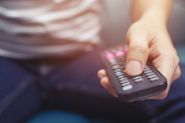 Close-up van de afstandsbediening van de televisie in casual man handen tv-toestel te wijzen en deze aan of uit te zetten. selecteer kanaal tv kijken op zijn bank thuis in de woonkamer ontspannen.