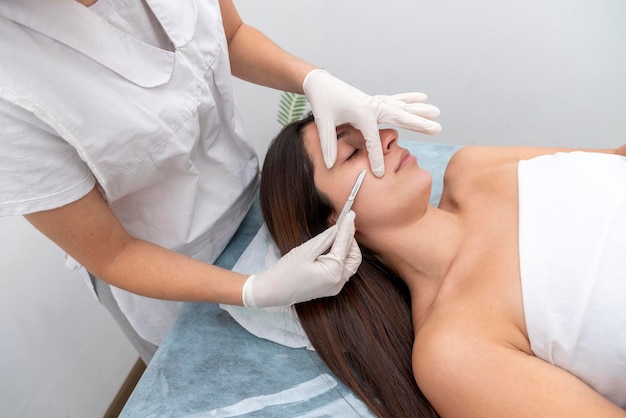 Close-up van de arts met een scalpel die de huid van de vrouw behandelt. Dermaplaning-behandeling.