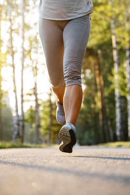 Close-up van de benen van een atleet met grijze sneakers die op een onverharde weg lopen in de kuitspieren van het park in het werk