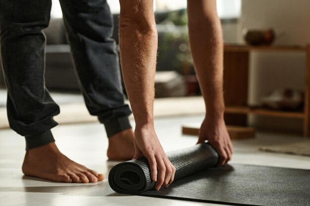 Close-up van de blootvoetse man die mat voorbereidt op yoga-oefeningen in de kamer thuis