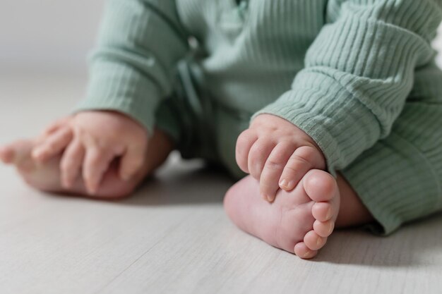 Close-up van de blote voeten van een baby in een groene jumpsuit die op de vloer zit