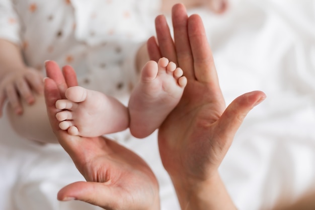 Close-up van de blote voeten van een pasgeboren baby in zijn moeders handen op een witte achtergrond bovenaanzicht