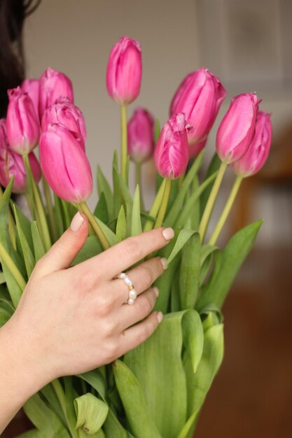 Close-up van de details van de verfraaide handen van het meisje met juwelen die roze bloemen houden