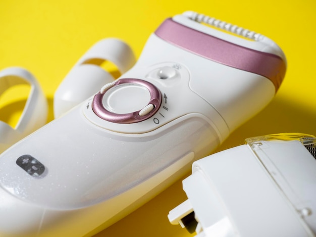 Close-up van de elektrische epilator voor ontharing van witte kleur op een gele achtergrond. Naast het extra mondstuk. Schoonheidsproducten voor het behouden van schoonheid