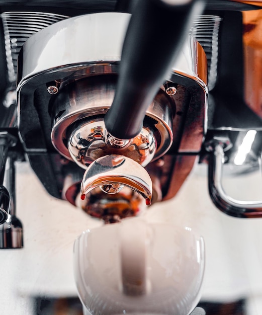 Close-up van de extractie van koffiedruppels uit de koffiemachine met een portafilter die koffie giet