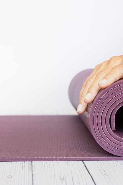 Close-up van de hand die van een vrouw een violette yogamat op witte houten oppervlakte opent