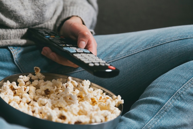 Foto close-up van de hand met de afstandsbediening van tv en popcorn. filmavond thuis