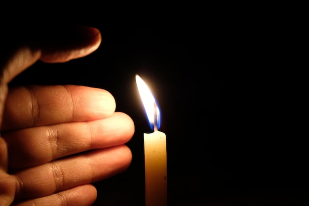Close-up van de hand met een brandende kaars tegen een zwarte achtergrond