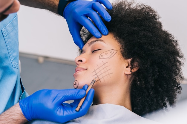 Close-up van de hand van de arts die correctielijnen trekt op het gezicht van de jonge vrouw. procedure vóór plastische chirurgie.