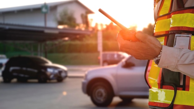 Close-up van de hand van de bewaker in een veiligheidsvest met behulp van walkie talkie op de parkeerplaats buiten