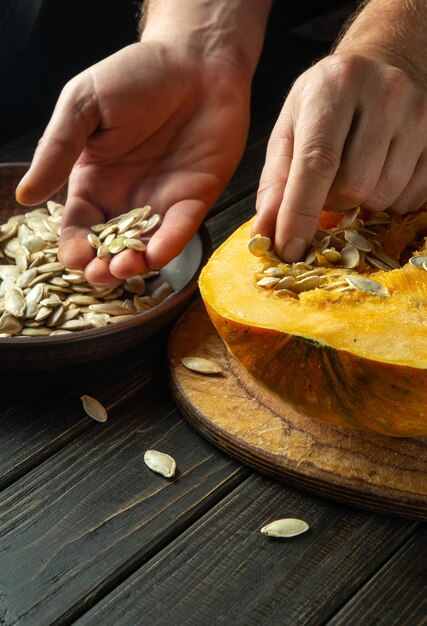 Close-up van de hand van de man die zaden uit de pompoen trekt na de oogst Zoren oogsten voor gebruik bij het koken