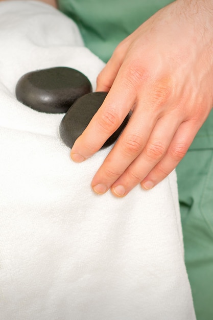 Close-up van de hand van de masseur veegt zwarte massagestenen af met een witte handdoek.