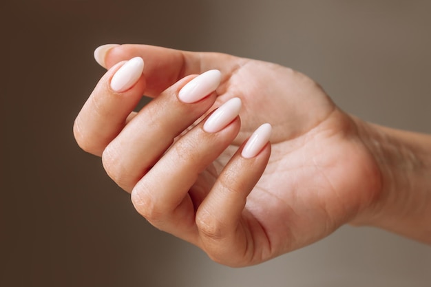 Close-up van de hand van de vrouw met een perfecte natuurlijke neutrale delicate manicure op een donkerbruine achtergrond