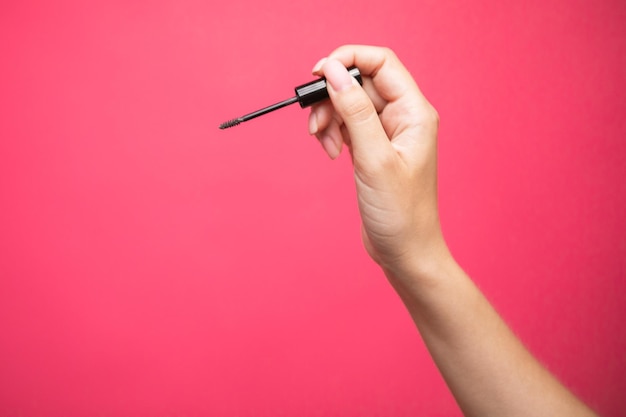 Close up van de hand van de vrouw met een wenkbrauwen borstel mascara op roze achtergrond