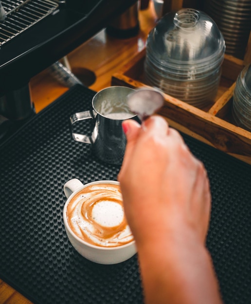 Close-up van de hand van een barista in de coffeeshop die zich voorbereidt op het stomen van melk voor een kopje cappuccino