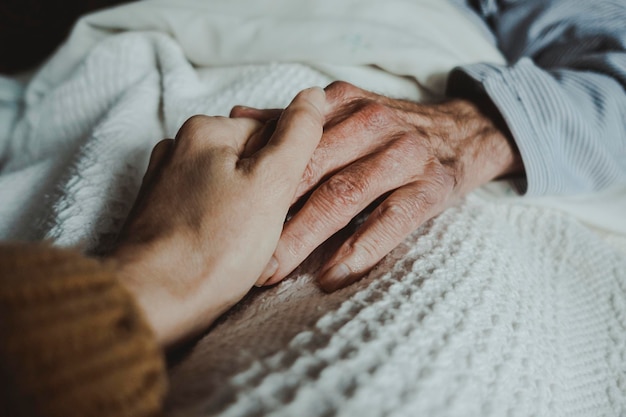 Close-up van de hand van een jonge vrouw die de hand vasthoudt van een oude man die op een bed ligt