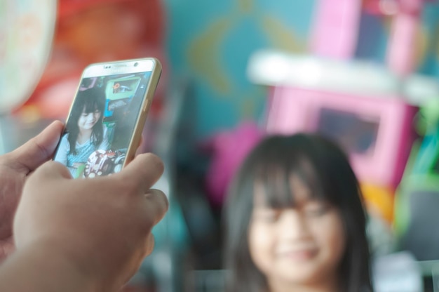 Close-up van de hand van een man die zijn dochter met een mobiele telefoon fotografeert