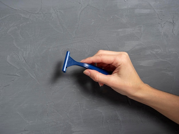 Close-up van de hand van een vrouw met een blauw plastic scheermes op een grijze gestructureerde achtergrond