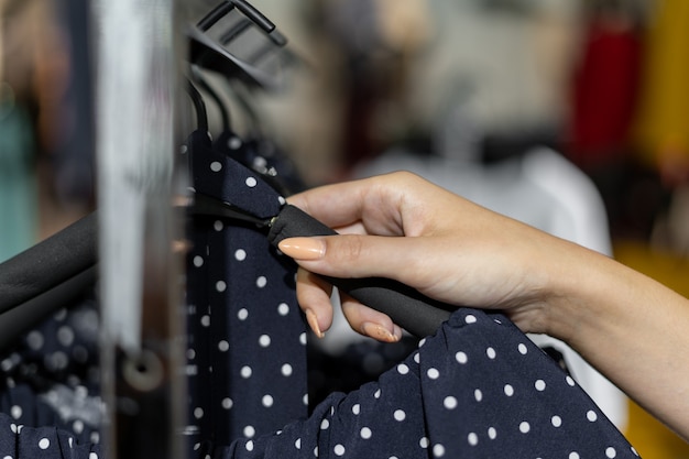 Close-up van de hand van een vrouw trekt een jurk uit van een hanger. Winkelconcept voor dameskleding.