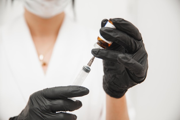 Close-up van de handen van de arts in beschermende steriele handschoenen die een spuit uit een ampul met een vaccin nemen Witte achtergrondruimte voor tekst