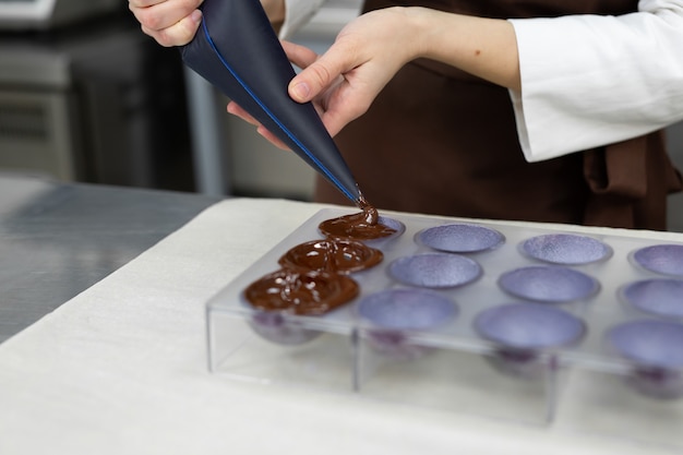 Close-up van de handen van de chocolatiers die chocolade in de vormen gieten