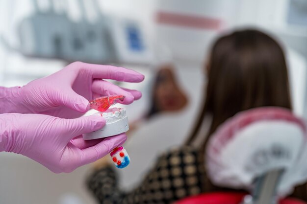 Close-up van de handen van de dokter in blauwe handschoenen houden een kunstmatig model van de kaak vast met pauzes De tandarts toont een voorbeeld van tanduitlijning