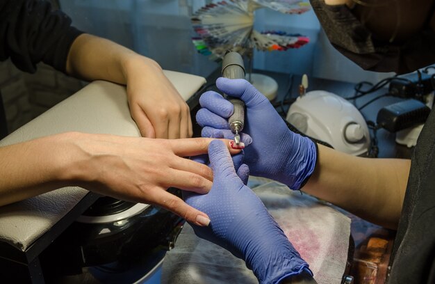 Close-up van de handen van de meester die hardwaremanicure doet aan de klant