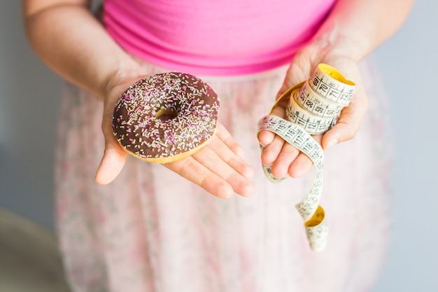 Close-up van de handen van de vrouw met een donut en een meetlint. Het concept van gezond eten. Eetpatroon.