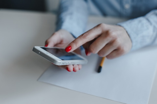 Close-up van de handen van de vrouw met rode nagels die mobiele telefoon houden en klikken die online betalen en chatten die blauw overhemd dragen.