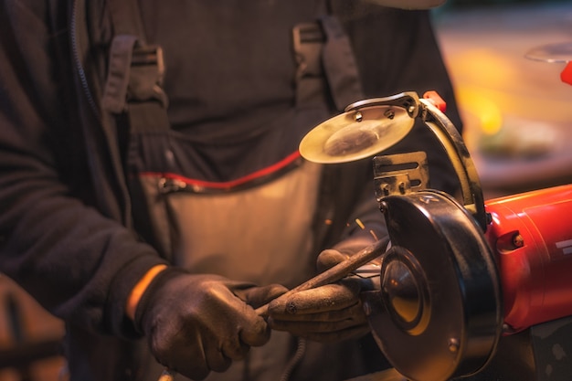 Foto close-up van de handen van een arbeider in zwarte handschoenen die aan een metaaldeel op een rode malende machine werken