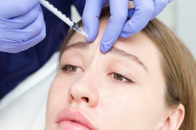 Close-up van de handen van een deskundige schoonheidsspecialist die botox injecteert in het voorhoofd van een vrouw Correctie van voorhoofd- en oogrimpels met botulinumtoxine