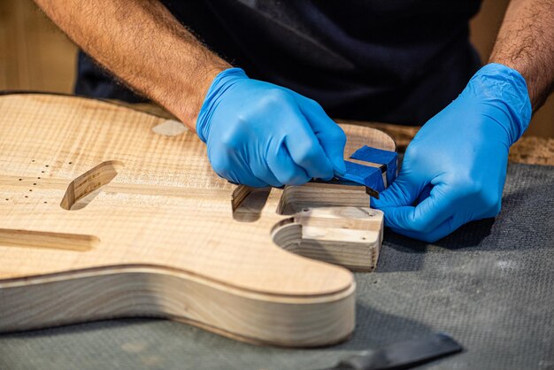 Close-up van de handen van een gitaarbouwer aan het werk op het lichaam van een gitaar, handen van een vakman met beschermende handschoenen, muziekzaken en de bouw van muziekinstrumenten