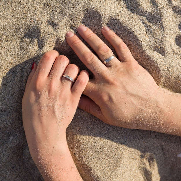 Close-up van de handen van een jonge vrouw en man tegen de achtergrond van zand