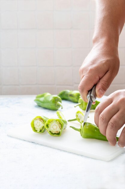 Close-up van de handen van een man die lange groene paprika's snijden om te beginnen met koken