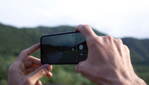 Foto close-up van de handen van een man met een smartphone en neem een foto van het landschap