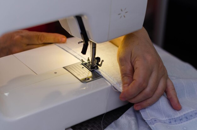 Close-up van de handen van een naaister die witte stof op een naaimachine naait