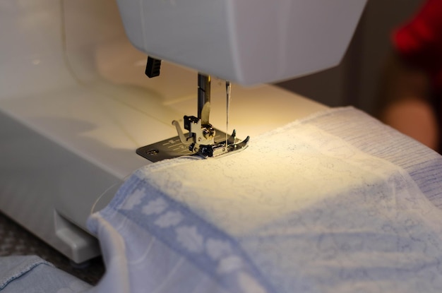 Close-up van de handen van een naaister die witte stof op een naaimachine naait