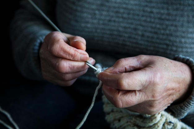 Close-up van de handen van een oudere vrouw die een trui breien