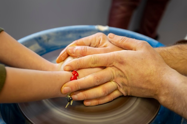 Close-up van de handen van een pottenbakker en de hand van een kind met een voorwerp op een pottenbakkersschijf