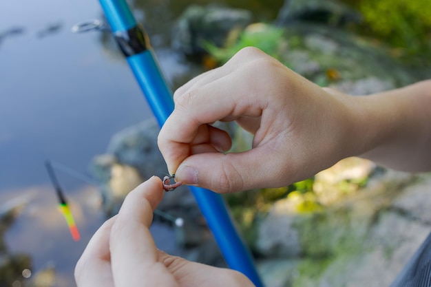 Close-up van de handen van een tiener die aas op een vishaak legt Sportvissen op de rivier in de zomer