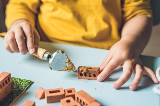 Close up van de handen van het kind spelen met echte kleine bakstenen aan de tafel