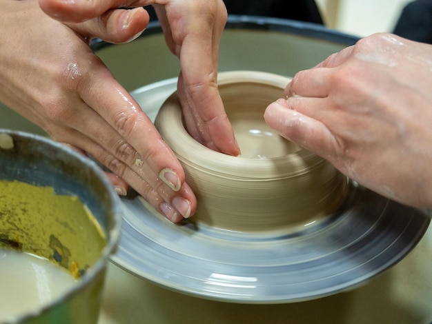 Close-up van de handen van mensen die een object maken van ruwe klei op een pottenbakkersschijf Masterclasses en workshops gehouden Hobby selectieve focus