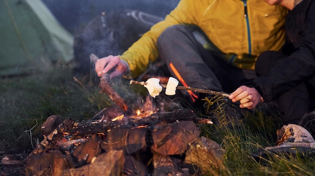 Close-up van de handen van mensen die stokken met marshmallow buiten in de buurt van kampvuur houden