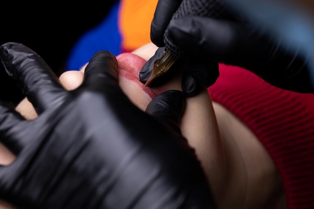 Close-up van de meester in zwarte steriele handschoenen veegt de overblijfselen van het tatoeagepigment van de lippen van het model met wattenstaafjes
