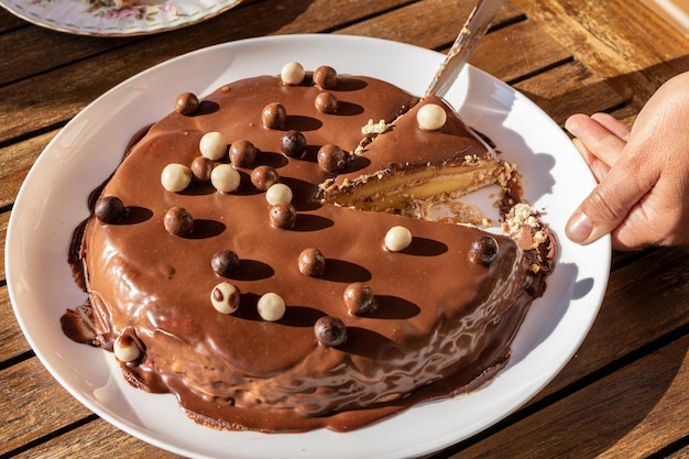 Close-up van de menselijke hand die een portie zelfgemaakte chocoladetaart snijdt met daarop witte chocoladeballen