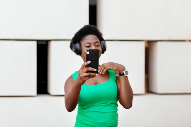 Foto close-up van de telefoon in de handen van een afrikaans meisje dat naar muziek luistert in een draadloze koptelefoon op haar mobiele telefoon, danst en een selfie maakt.