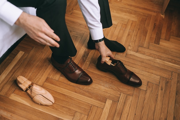 Close-up van de voeten van de bruidegom of zakenman die nieuwe stijlvolle schoenen aantrekt. Mannenhanden halen houten inzetstukken uit schoenen. Mensen, zaken, mode en schoenenconcept.