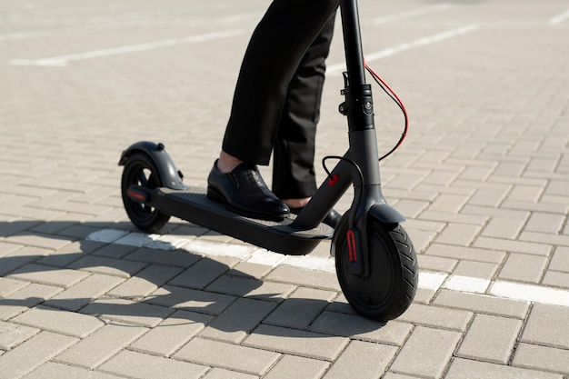 Close-up van de voeten van een man in een pak en schoenen in de buurt van een elektrische scooter