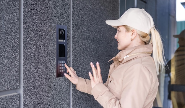 Close-up van de vrouwelijke hand drukt op de deurtelefoon-knop. Het meisje belt de intercom. Communicatiemiddel of melding van aankomst en beveiliging van de ingang binnen.